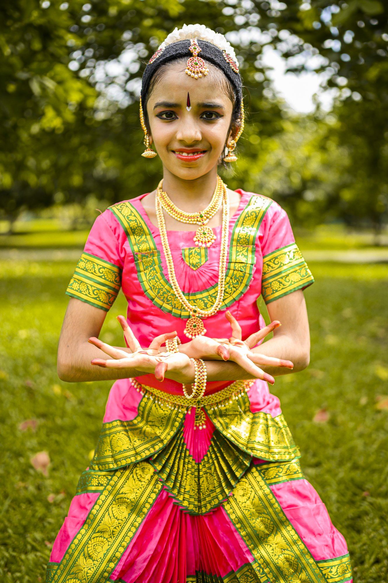 A young dancer in pink and green costume showing a mudra