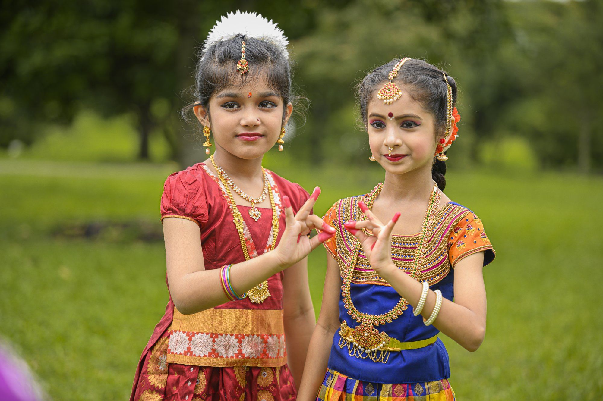 Two young students in red and orange costumes showing mudras