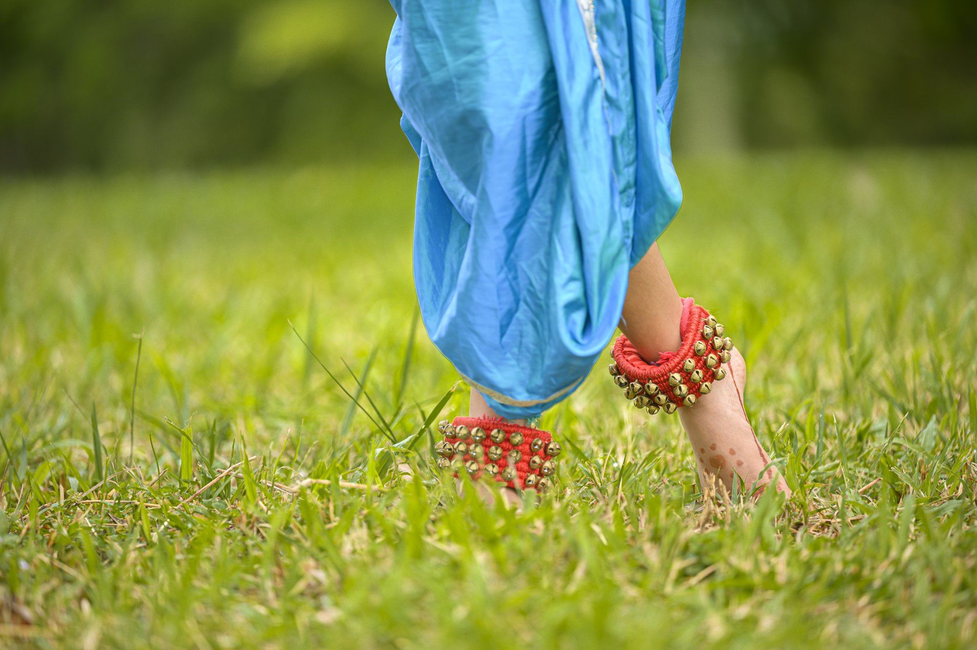 Close-up of a dancer's feet wearing salangai ankle bells on the grass